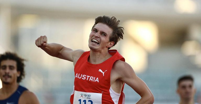 Ein männlicher Athlet aus Österreich läuft bei einem Leichtathletikwettbewerb und trägt ein rotes Puma-Trikot mit der Nummer 112. Er feiert mit einer Faustpumpe.
