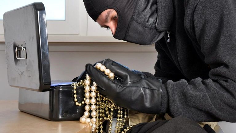 Eine maskierte Person, die schwarze Handschuhe trägt, hält eine Sammlung von Perlenketten und Goldketten.