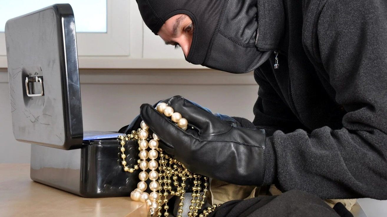 Eine maskierte Person, die schwarze Handschuhe trägt, hält eine Sammlung von Perlenketten und Goldketten.