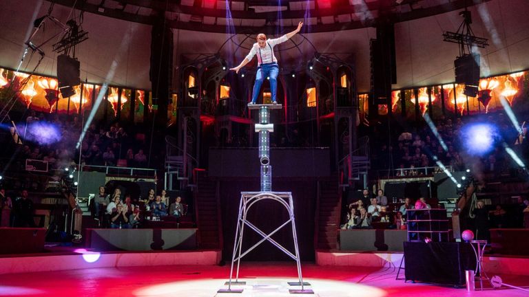 Ein Mann balanciert auf der Spitze einer hohen Metallstruktur während einer Aufführung in einem Theater.
