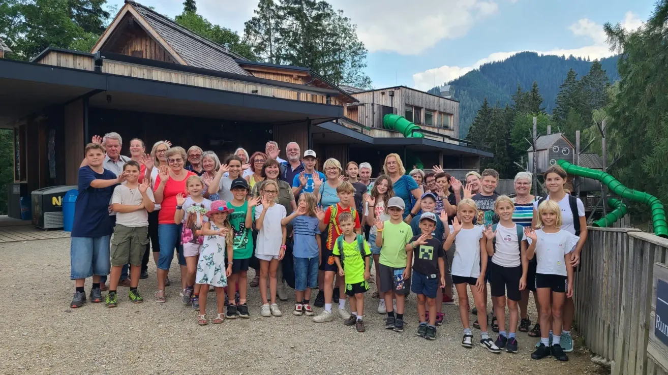 Eine Gruppe von Menschen, einschließlich Erwachsener und Kindern, posiert für ein Foto vor einem Gebäude mit einem Berg im Hintergrund.