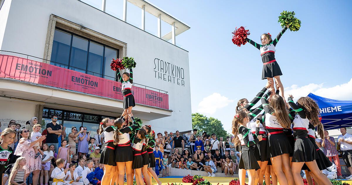 Eine Gruppe Cheerleader führt vor einer Menge im Stadtkino Theater eine Stunt-Darbietung durch. Sie halten sich gegenseitig hoch, um eine Pyramide zu bilden.
