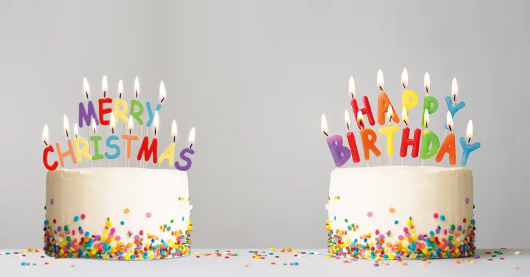 Zwei Geburtstagskuchen mit bunten Streuseln und Kerzen, einer mit 'Frohe Weihnachten' und der andere mit 'Alles Gute zum Geburtstag' obenauf geschrieben.