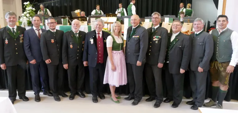 Eine Gruppe von Menschen in Uniformen, einschließlich Militär- und traditioneller Kleidung, steht für ein Foto zusammen. Eine Frau in einem rosa Kleid steht in der Mitte.