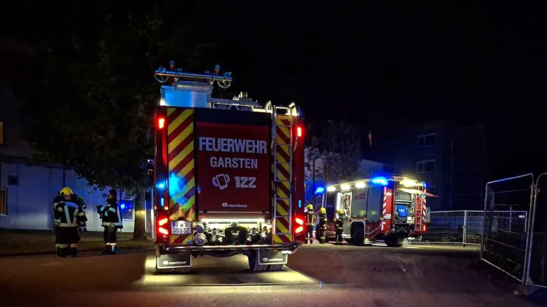Ein Feuerwehrauto mit der Nummer 122 aus Garsten steht nachts mit eingeschalteten Lichtern, Feuerwehrleute sind in der Nähe.