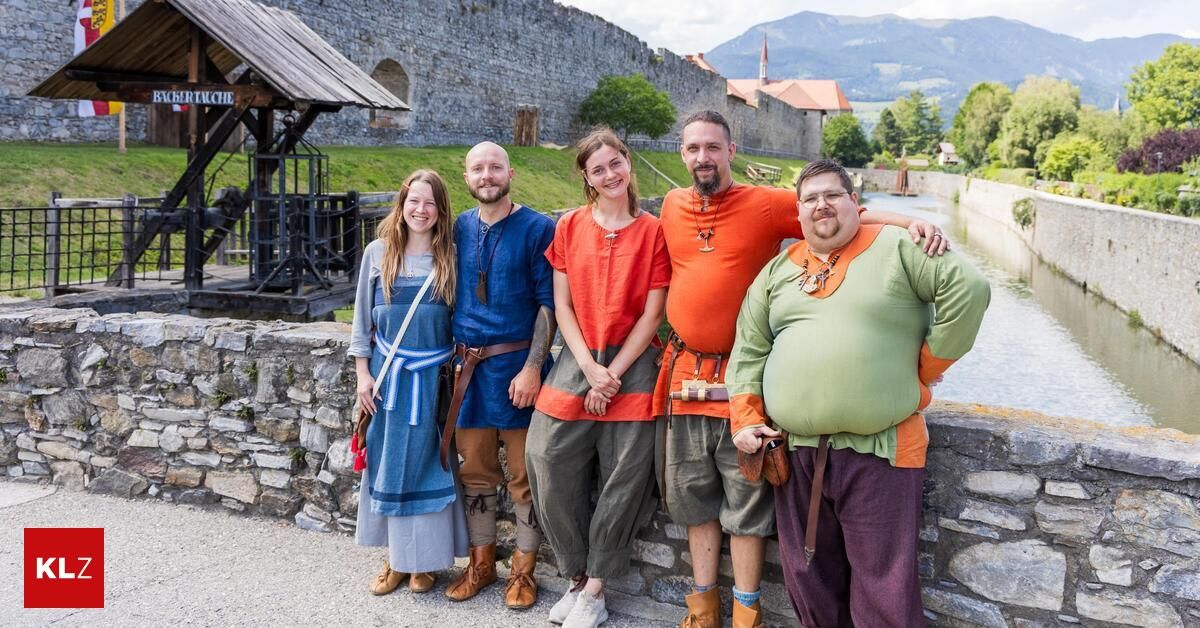 Fünf Menschen in mittelalterlicher Kleidung posieren für ein Foto vor einer Steinmauer und einer Burg im Hintergrund.