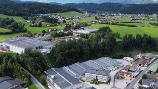 Ein Luftbild eines großen Industriekomplexes mit mehreren Gebäuden, umgeben von grünen Feldern und einem kleinen Dorf in der Ferne.