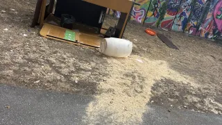 Ein umgestürzter Holzschreibtisch mit verstreutem Sägemehl liegt am Boden, in der Nähe einer mit Graffiti bedeckten Wand.