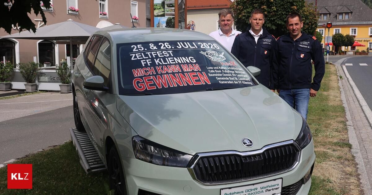 Vier Männer in Uniformen stehen neben einem Auto mit einem Schild, das 'Zeltfest FF Kleining 25. & 26. Juli 2026' und 'Mich kann man gewinnen' auf der Windschutzscheibe steht. Das Auto ist auf Gras geparkt.