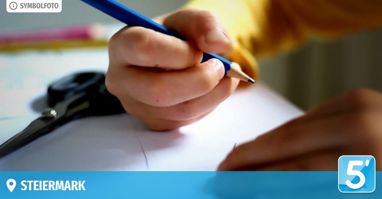 Ein Nahaufnahme der Hand eines Kindes, das einen blauen Stift hält und auf einem Blatt Papier schreibt. Die Hand ist leicht verschwommen, mit einem gelben Shirt im Hintergrund.