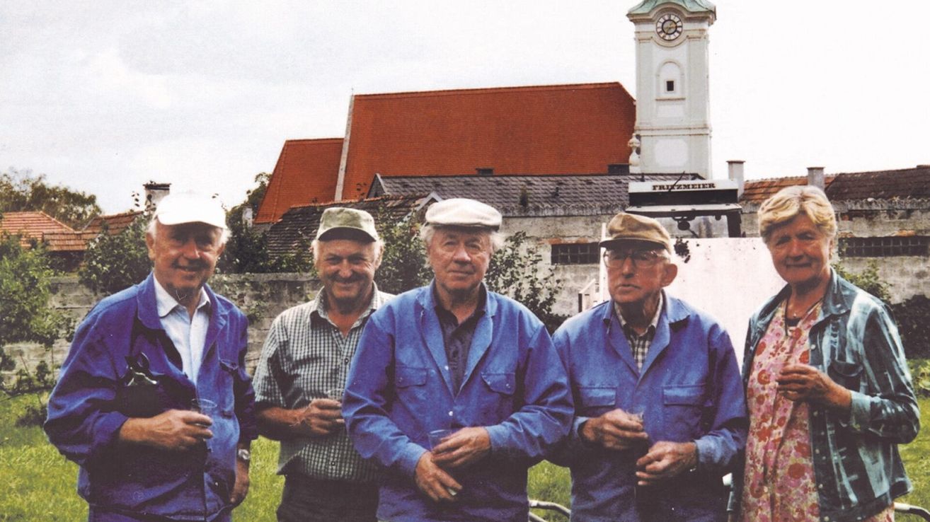 Vier ältere Männer in blauen Arbeitsuniformen stehen vor einem Gebäude mit einem Uhrturm.