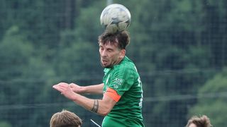 Ein Fußballspieler in einem grünen Trikot mit einem Fußball auf dem Kopf balanciert.