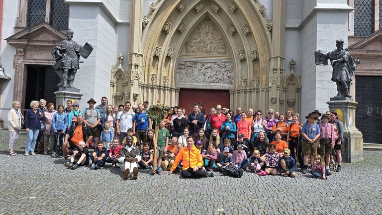 Eine große Gruppe von Menschen, einschließlich Erwachsener und Kindern, posiert für ein Foto vor einer Kirche mit kunstvollen architektonischen Details.