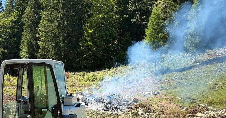 Ein Fahrzeug ist auf einem Hang geparkt, mit Rauch, der aus einem Feuer im Vordergrund aufsteigt.