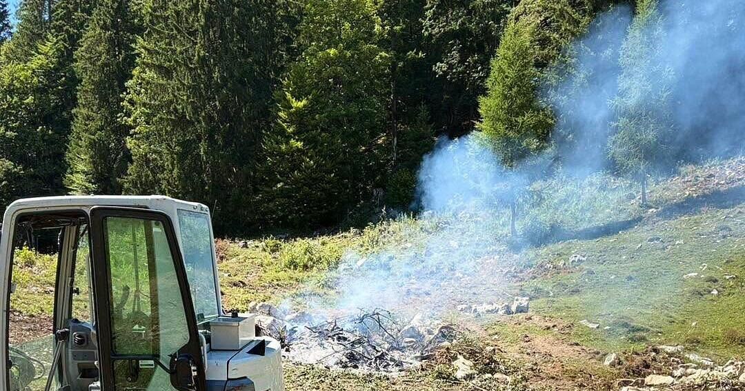 Ein Fahrzeug ist auf einem Hang geparkt, mit Rauch, der aus einem Feuer im Vordergrund aufsteigt.