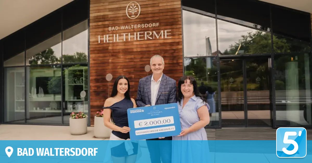 Drei Personen stehen vor einem Gebäude mit dem Schild Bad Waltersdorf Heiltherme. Der Mann und die beiden Frauen lächeln und halten einen großen blauen Scheck über 2.000 Euro.