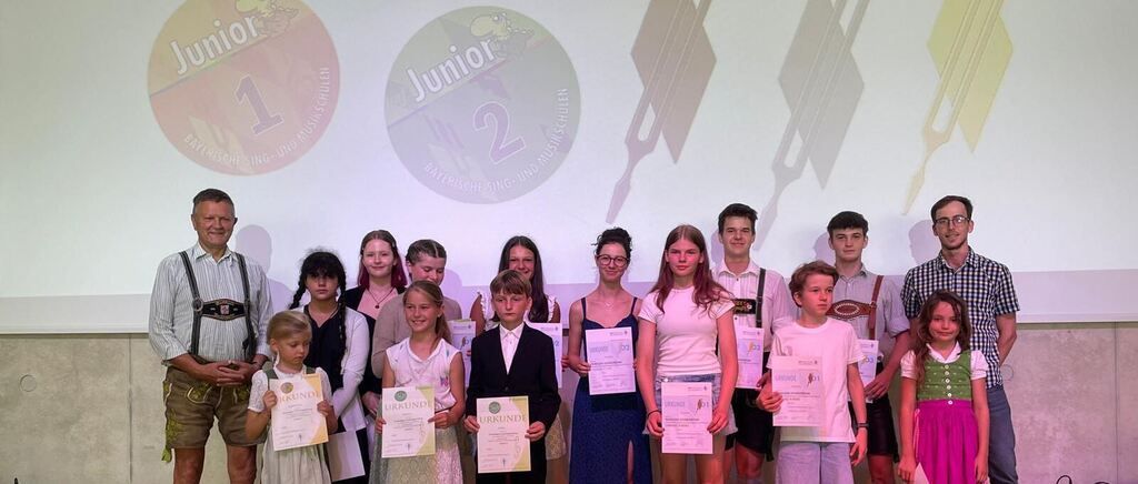 A group of young people and adults are posing for a photo with certificates in hand, standing in front of a backdrop with logos and text.