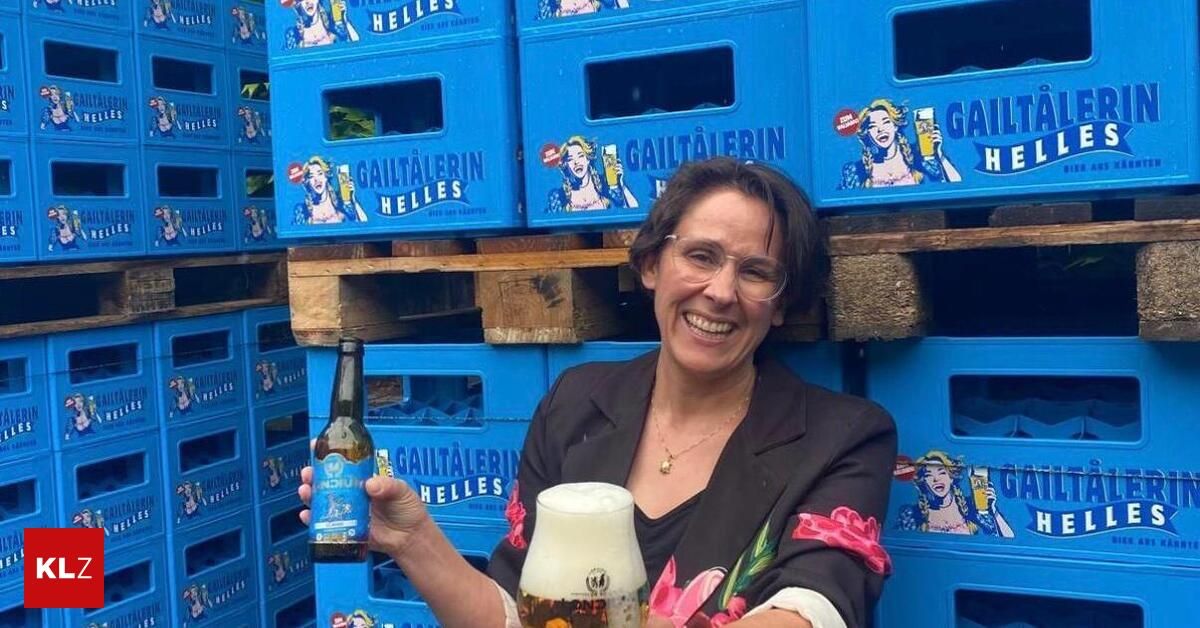 A woman wearing glasses and a black blazer holds a bottle of beer and a glass of beer in front of blue crates labeled 'Gaultaleerin Helles'.