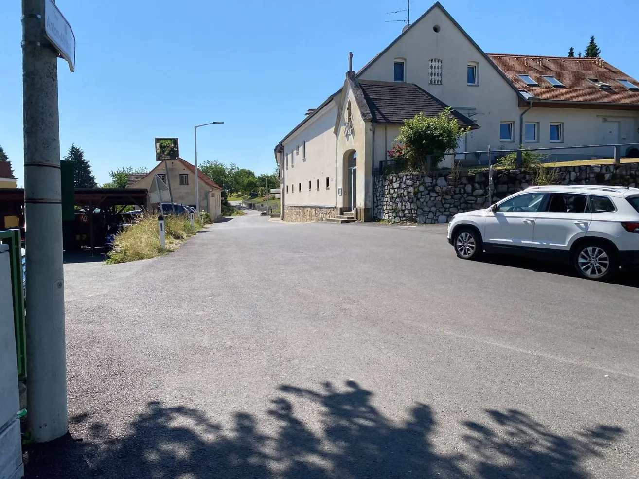 Ein weißer SUV ist auf einer Straße geparkt, mit einem großen weißen Gebäude im Hintergrund. Das Gebäude hat ein braunes Dach und mehrere Fenster.