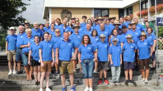 A group of people in blue shirts and hats are posing for a photo on the steps of a building.