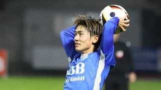 A soccer player in a blue jersey with the letters SB and GmbH on it, holding a soccer ball with both hands.