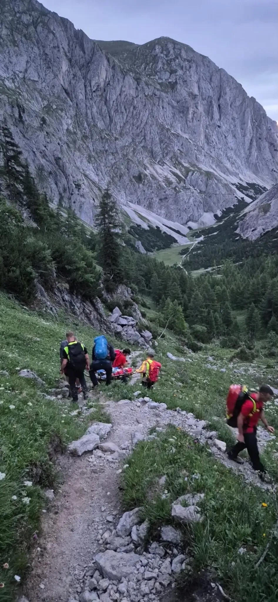 Eine Gruppe Bergretter trägt eine Person auf einer Trage den steilen Bergpfad hinunter.