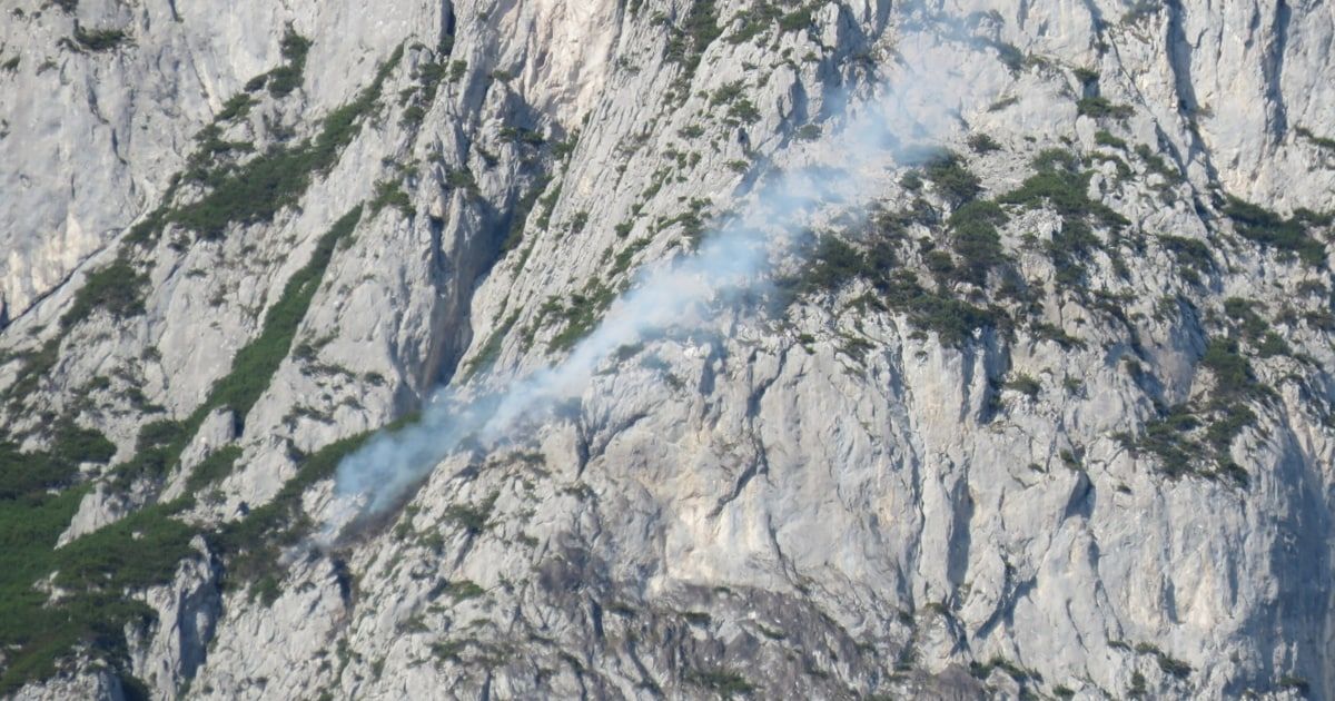 A mountain with a smoke trail on its side, indicating a fire or disturbance.