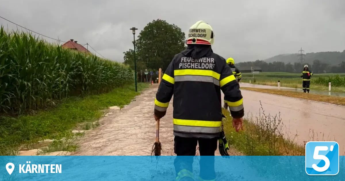 A firefighter from Pischeldorf is walking on a muddy path, holding a broom, wearing a reflective jacket and helmet.
