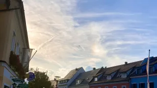 Eine Straßenansicht einer kleinen Stadt mit Gebäuden auf beiden Seiten, geparkten Autos am Straßenrand und einem blauen Himmel mit Wolken.