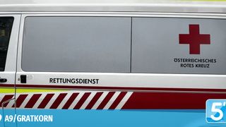Eine Nahaufnahme der grauen und roten Fahrzeugseite mit den Worten 'Rettungsdienst' und 'Oster Rot'. Das Fahrzeug hat einen weißen Streifen am unteren Rand.