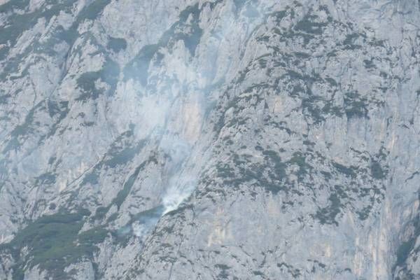 A mountain with a small fire burning on its side, surrounded by rocky terrain and sparse vegetation.