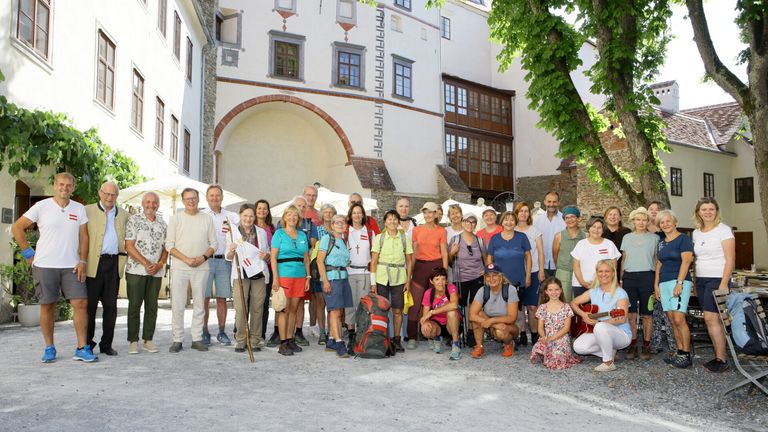 A group of people, likely tourists, pose for a photo in front of a historic building with arched windows and a tree.