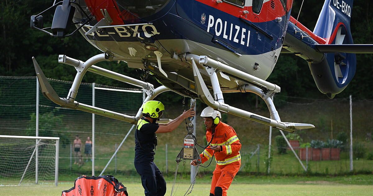 Two men in safety gear, one in black and one in orange, are securing a helicopter with ropes. The helicopter has 'POLIZEI' written on its side.