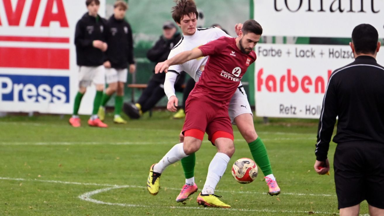 Zwei Fußballspieler in roten und weißen Trikots kämpfen auf einem Feld um den Ball.
