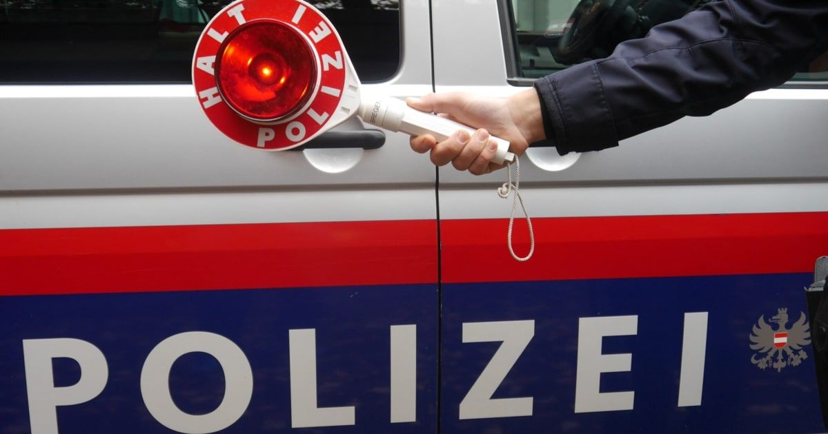 Die Hand eines Polizisten, der ein blinkendes rotes Licht mit dem Wort 'POLIZEI' an einem Polizeifahrzeug hält.