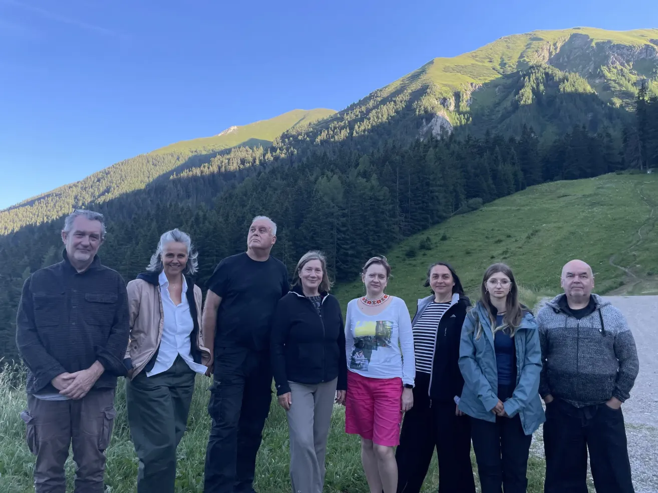 A group of people standing in front of a mountain with a clear blue sky. They are smiling and posing for a photo.