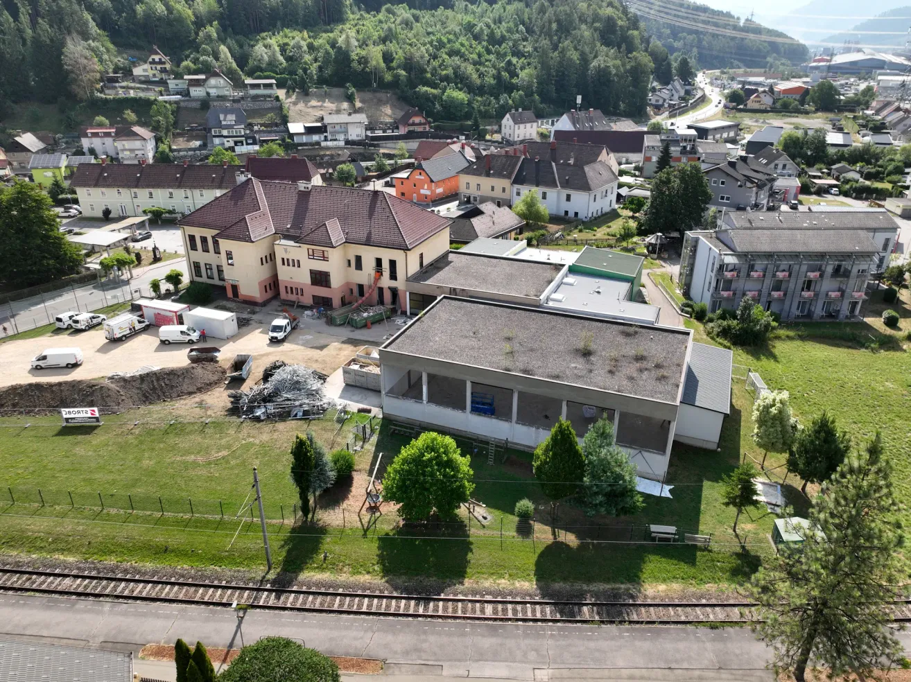 Ein Luftbild einer kleinen Stadt mit verschiedenen Gebäuden, einige im Bau, vor dem Hintergrund von üppigem Grün und sanften Hügeln.