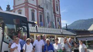 A group of elderly tourists stands in front of a historic building with a bus in the background.