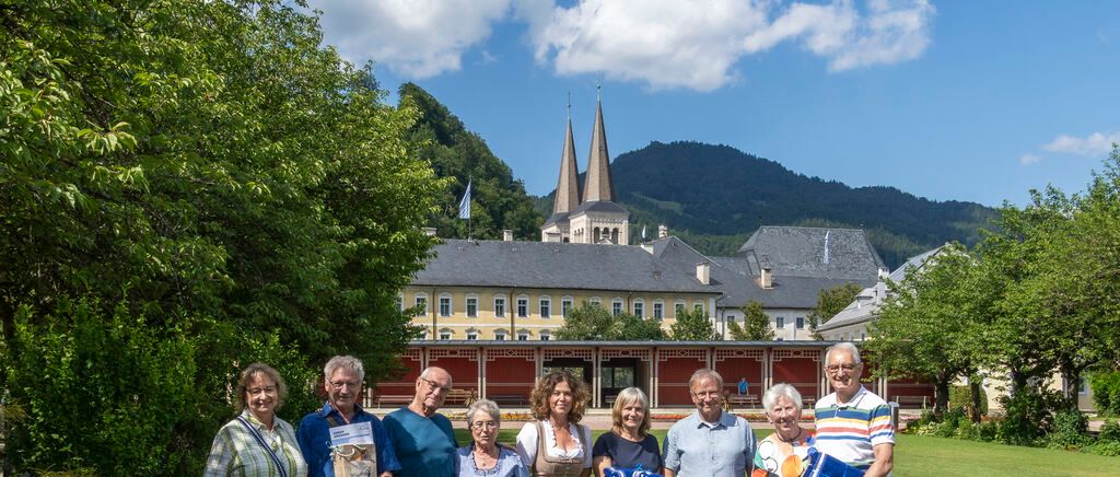 A group of people are standing in front of a building with a mountain in the background.