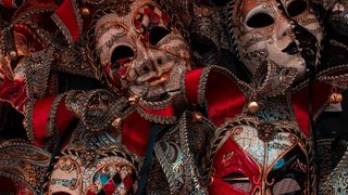 A collection of ornate masks with intricate designs and musical notes, some featuring red and gold accents, arranged closely together.