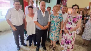A group of elderly people, including men and women, are standing together in a room. They are all smiling and appear to be posing for a photo.