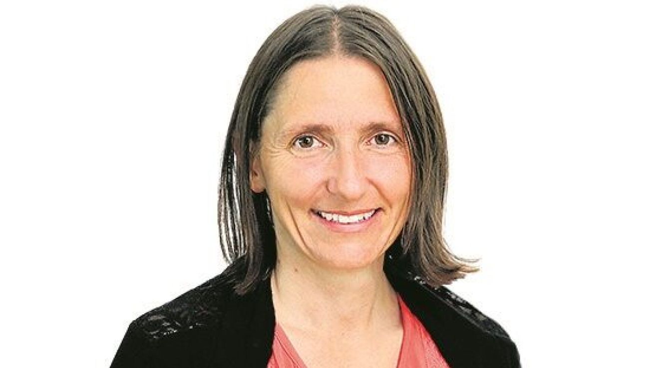 Eine Frau mit kurzen braunen Haaren und einem rosa Oberteil lächelt in die Kamera. Sie trägt eine schwarze Jacke.