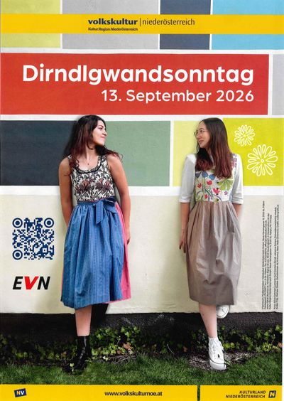 Zwei Frauen stehen neben einer bunten Wand, eine trägt ein Blumenkleid und die andere ein blaues Kleid mit einem QR-Code und dem Text 'Dirndlgwandsonntag 13. September 2026'.