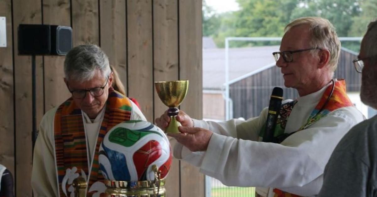 Two men in clerical attire hold a golden chalice and a colorful soccer ball, likely during a religious ceremony.