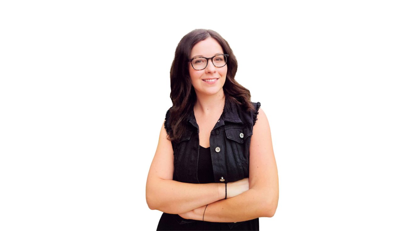 A woman with brown hair wearing glasses and a black vest, smiling and posing with her arms crossed.