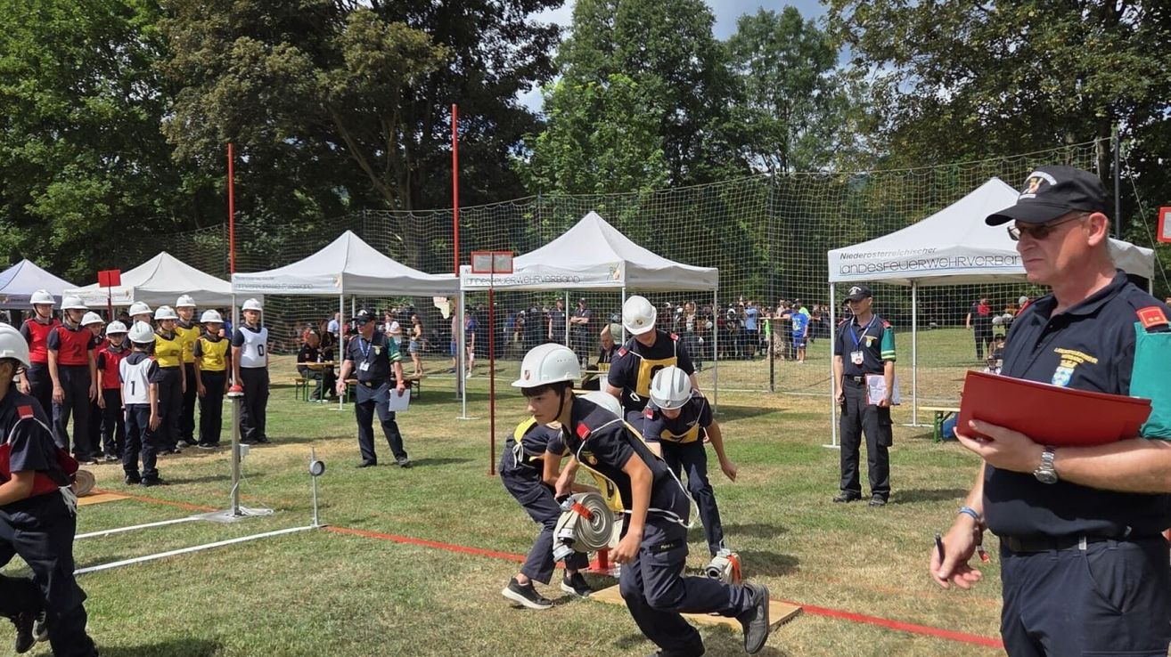 A group of young people in uniform are participating in a competition on a grassy field with tents and spectators in the background.