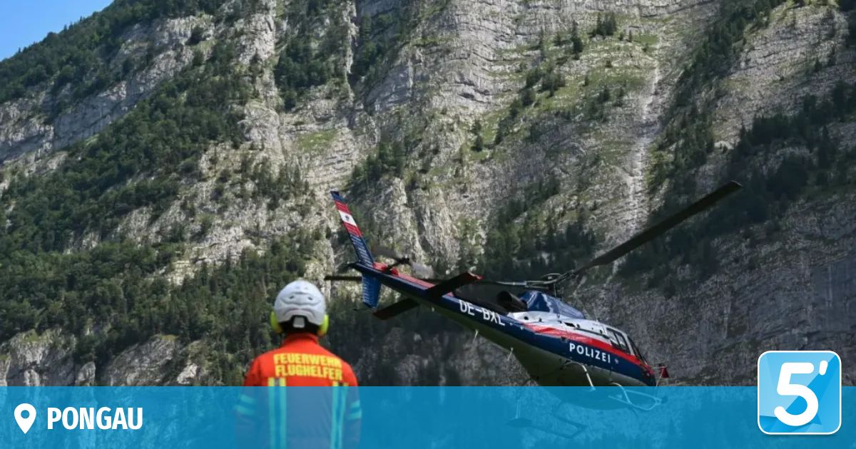 A firefighter in a red uniform stands in front of a helicopter with the text 'POLIZEI' on the side, against a backdrop of a mountainous landscape.