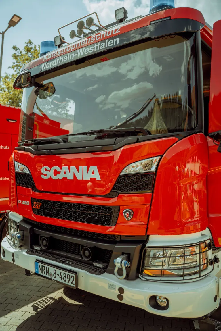Nahaufnahme der Vorderseite eines roten Scania-Lkws mit dem Wort Scania auffällig auf der Kühlergrill. Der Lkw hat ein Nummernschild und einen schwarzen Stoßfänger.