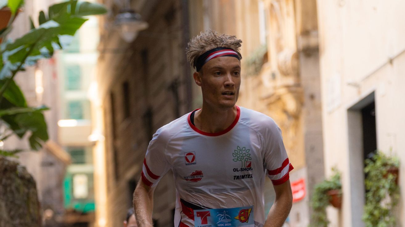 A man with a headband runs in a marathon, wearing a white shirt with red and white stripes and a red and white wristband.