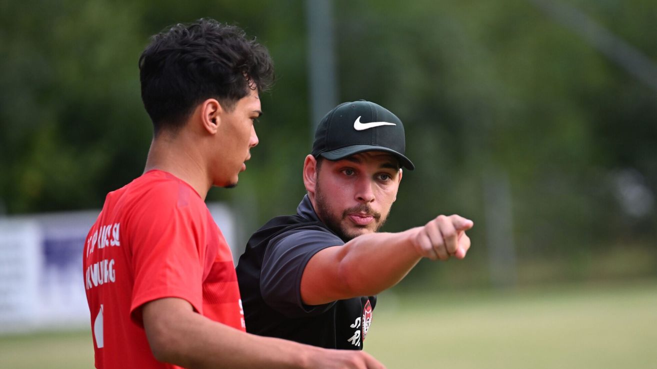 A man in a black Nike cap and shirt instructs a young man in a red shirt during a sports practice session.